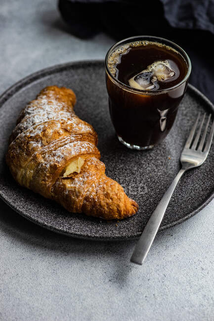 Nahaufnahme eines Eiskaffees mit einem frischen Vanille-Croissant auf einem Tisch — Stockfoto
