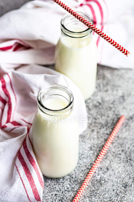Dos botellas de leche y pajitas para beber en la mesa junto a una toalla de té - foto de stock