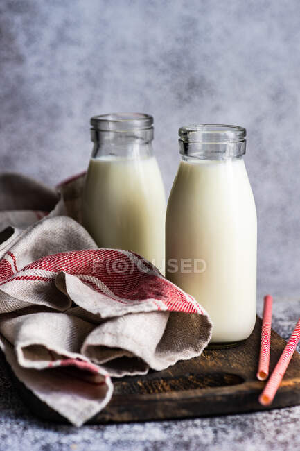 Duas garrafas de leite e palhinhas em uma tábua de corte de madeira com uma toalha de chá — Fotografia de Stock