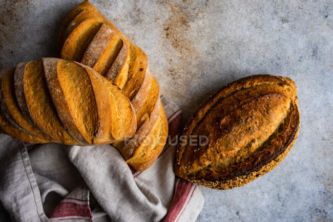 Overhead view of three loaves of freshly baked bread on a table next to a tea towel — Stock Photo