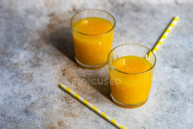 Dos vasos de jugo de naranja recién exprimido con pajitas para beber - foto de stock