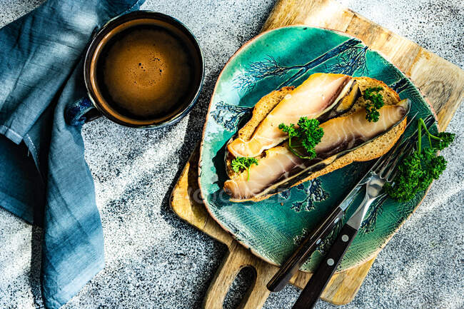 Overhead view of a slice of bread with smoked sturgeon and a cup of black coffee — Stock Photo