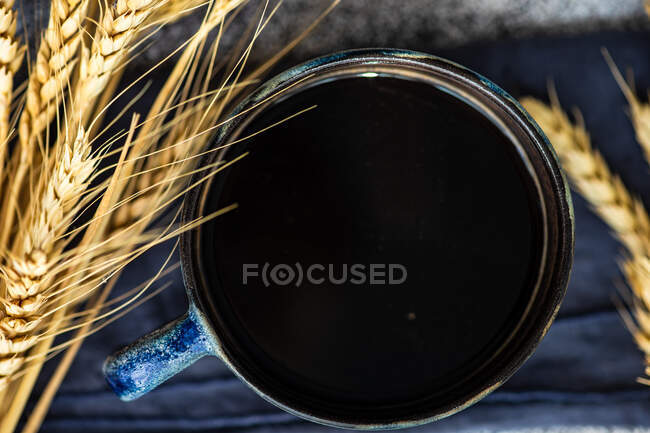 Vista aérea de una taza de café negro junto a espigas de trigo - foto de stock