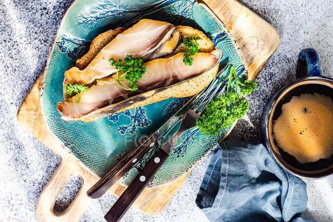 Slice of bread with smoked sturgeon and a cup of black coffee — Stock Photo