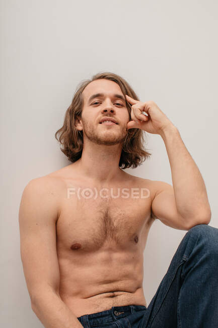 Portrait of a handsome shirtless man in jeans sitting on a table — Stock Photo
