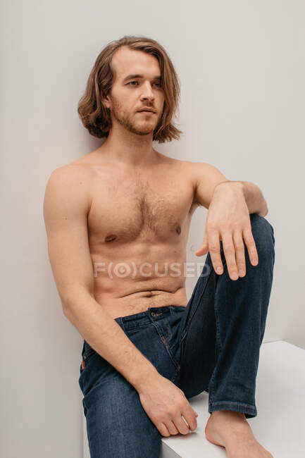 Portrait of a handsome shirtless man in jeans sitting on a table — Stock Photo
