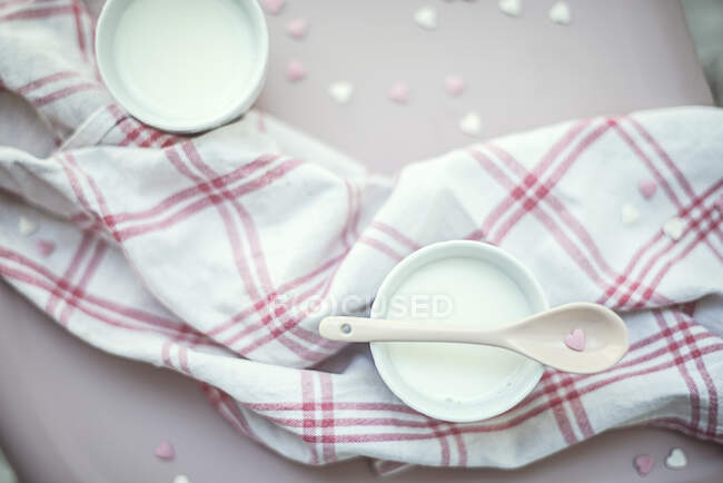 Overhead view of a cup of milk with heart shaped sprinkle decorations on the table and a tea towel — Stock Photo