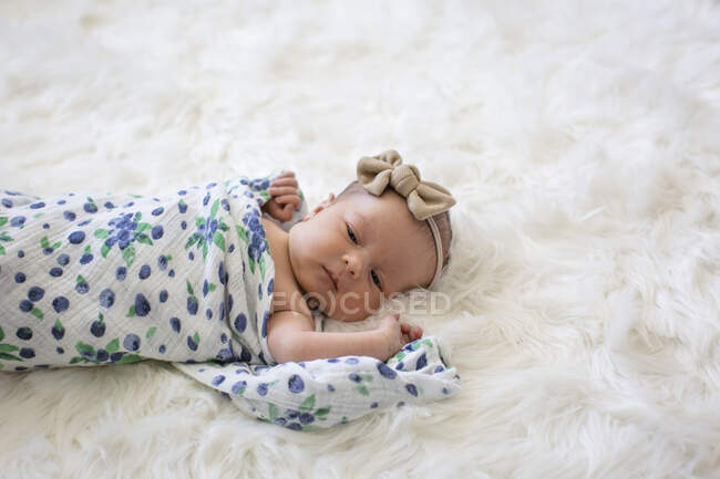 Nouveau-né bébé fille enveloppé dans la couverture couché sur moelleux tapis blanc — Photo de stock