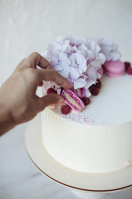 Bolo de decoração feminina mão com macaroon doce colorido e flores na mesa, vista de perto — Fotografia de Stock
