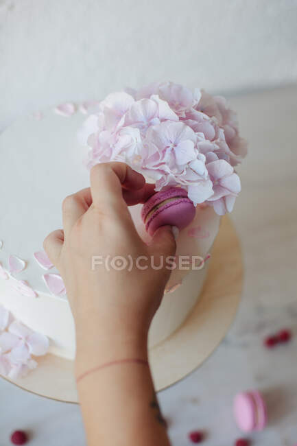 Female hand decorating cake with colorful sweet macaroon and flowers on table, close view — Stock Photo