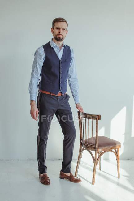 Homem vestindo roupas formais posando com cadeira em estúdio — Fotografia de Stock