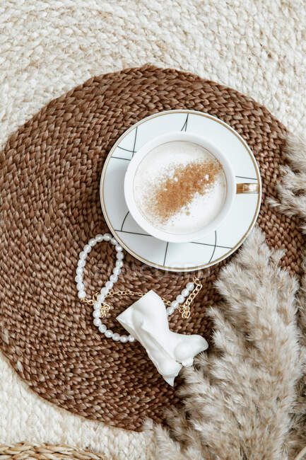 Close up of a cup of cappuccino with a knitted scarf and a book on a white background — Stock Photo
