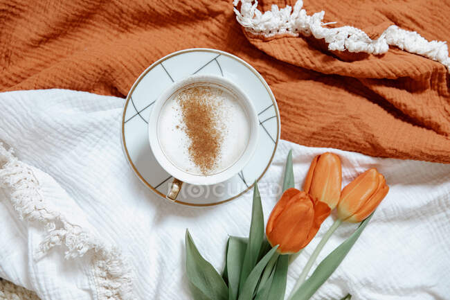 Tasse Kaffee mit roten Tulpenblüten am Tisch — Stockfoto