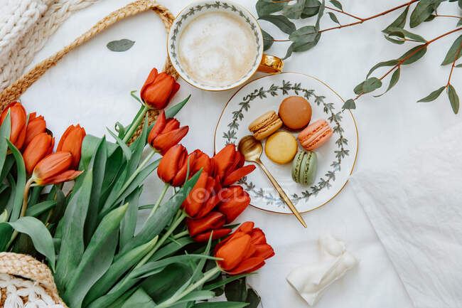 Taza de café y macarrones con flores de tulipán rojo en la mesa - foto de stock