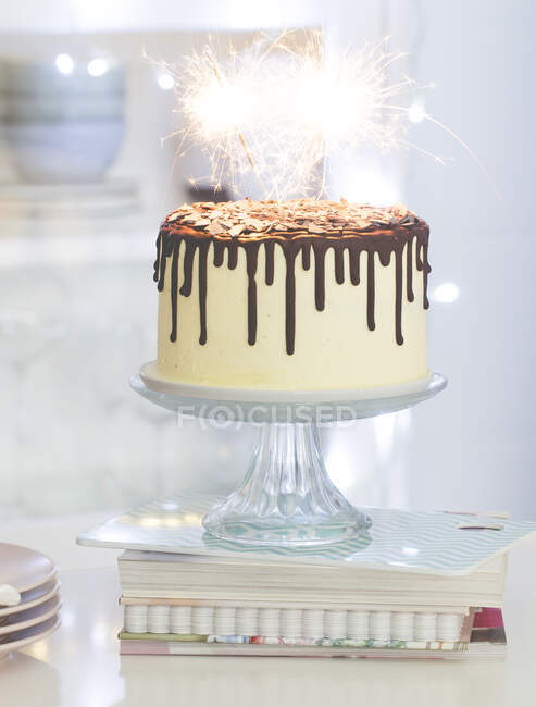 Vanilla birthday cake with chocolate ganache, glaze, and sparklers on a cake stand in a kitchen — Stock Photo