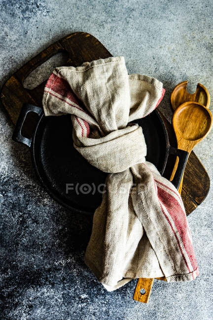 Концепция сельской кухни со старинной металлической сковородой и деревянными ложками, украшенными деревенским полотенцем — стоковое фото
