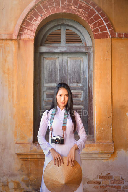 Beautiful woman standing in front of a window holding a traditional non la conical hat, Thailand — Stock Photo