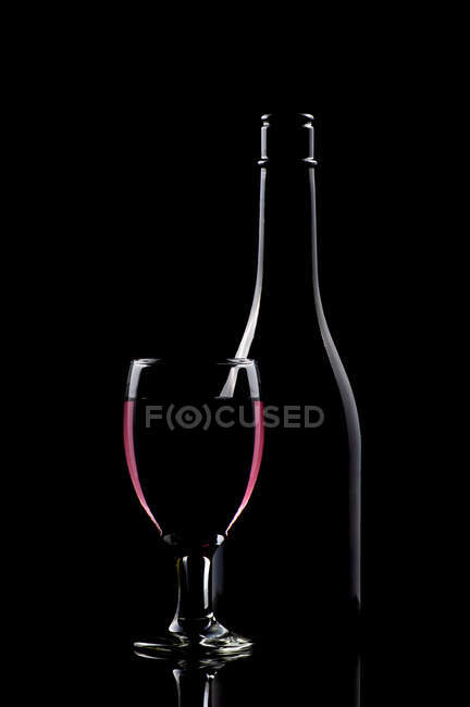 Copa de vino tinto junto a una botella en una mesa - foto de stock