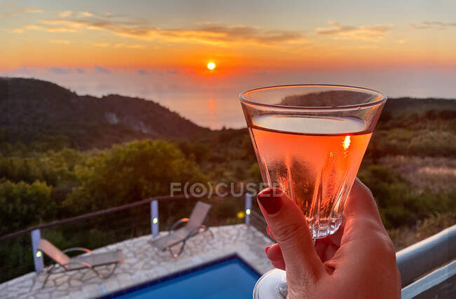 Жінка на балконі, насолоджуючись келихом вина на заході сонця в Лефкаді (Греція). — стокове фото