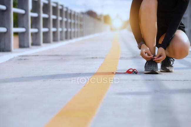 Corredor hembra agachada en un puente atándose los cordones de los zapatos, Tailandia - foto de stock