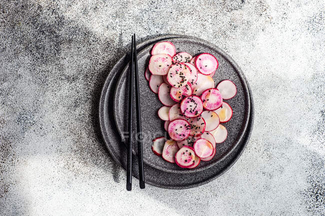 Органические свежие ломтики редьки на каменной тарелке с палочками для еды — стоковое фото