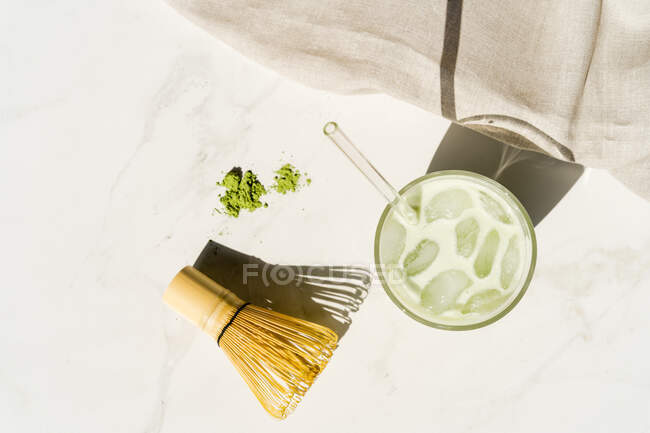 Vue aérienne d'une boisson de thé vert matcha glacée à côté de la poudre de matcha, du fouet de bambou et de la cuillère — Photo de stock
