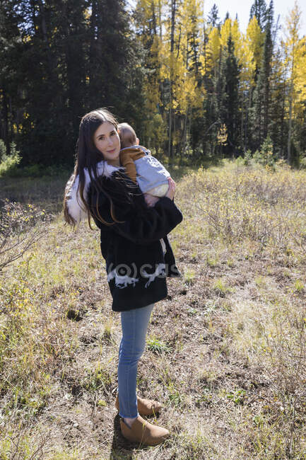Retrato de una mujer de pie en el bosque sosteniendo a su hija pequeña, California, EE.UU. - foto de stock