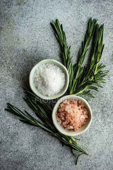 Stone bowls with salt spice and fresh rosemary herb on concrete table — Stock Photo