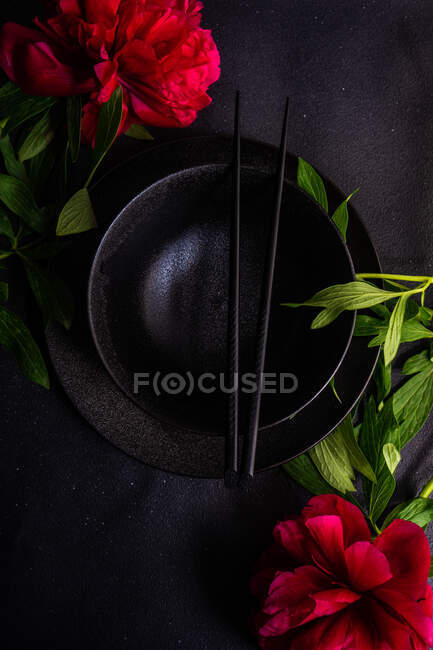 Cadre de table asiatique avec bol en céramique noire et chopstics décorés de fleurs de pivoine rouge — Photo de stock