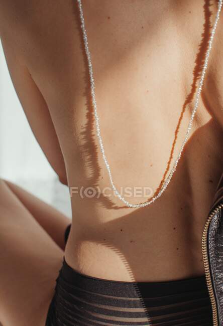 Rear view of a woman in lingerie wearing a necklace down her bare back — Stock Photo