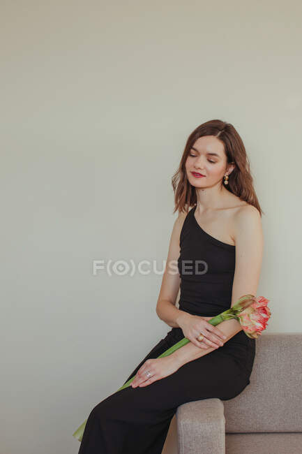 Portrait d'une belle femme en robe de soirée assise sur un canapé tenant une fleur Amaryllis — Photo de stock