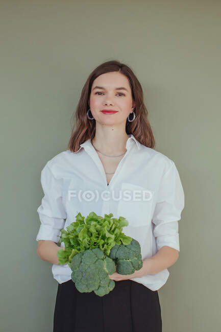 Portrait of a beautiful smiling woman holding fresh broccoli and lettuce — Stock Photo
