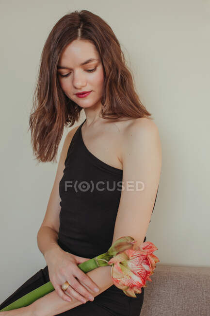 Portrait of a beautiful woman in an evening gown sitting on a sofa holding an Amaryllis flower — Stock Photo