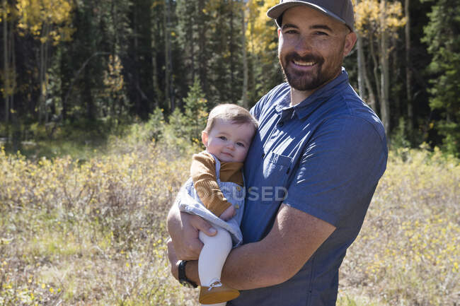 Retrato de un hombre sonriente sosteniendo a su hija en el bosque, California, EE.UU. - foto de stock