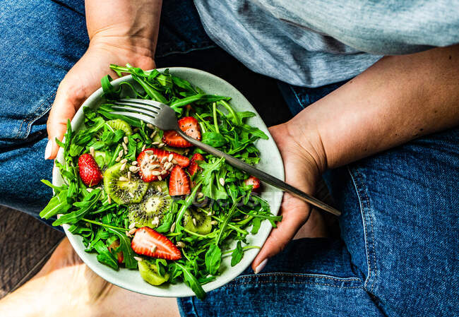 Frau isst gesunden Rucolasalat mit Erdbeeren und Kiwi — Stockfoto