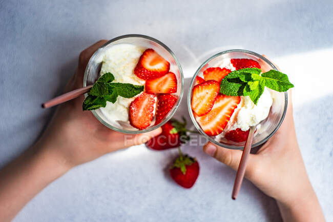 Dessert de crème glacée d'été servi avec des fraises et de la menthe dans les mains de l'enfant — Photo de stock