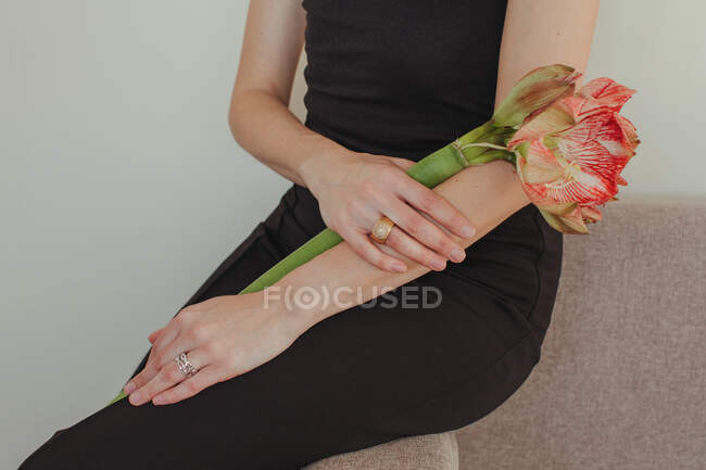 Close-up of a woman in an evening gown sitting on a sofa holding an Amaryllis flower — Stock Photo