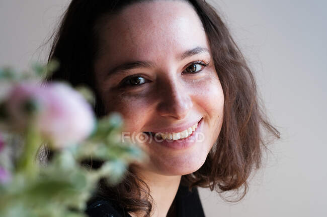 Portrait of a beautiful smiling woman standing by flowers — Stock Photo