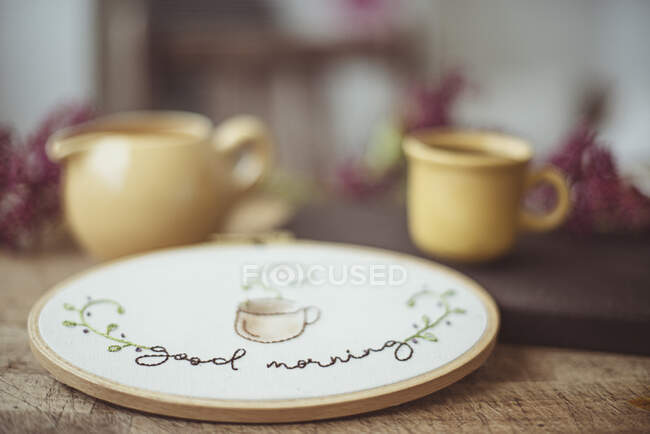 Stickrahmen mit einer Tasse Kaffee, Milchkanne und Blumen auf einem Tisch — Stockfoto