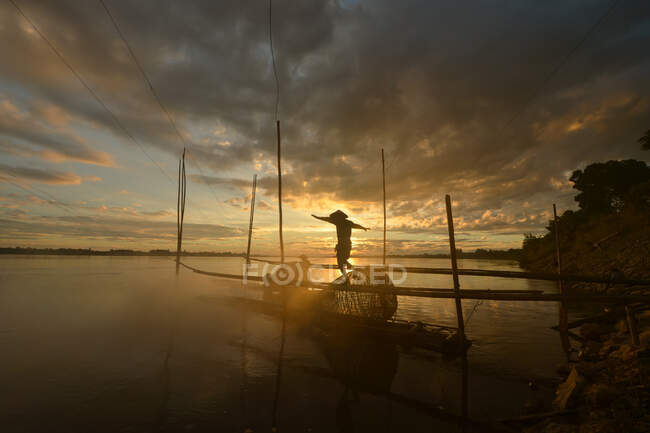 Silhouette di un pescatore che cammina lungo un molo al tramonto, Thailandia — Foto stock