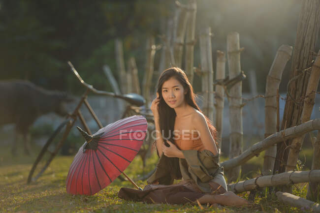 Mulher sentada na grama ao lado de seu guarda-sol, Tailândia — Fotografia de Stock