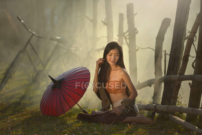 Donna seduta sull'erba accanto al suo ombrellone, Thailandia — Foto stock