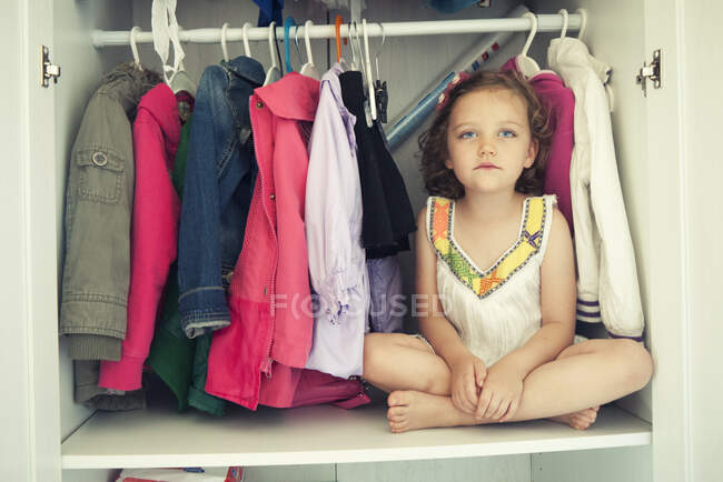 Chica sentada con las piernas cruzadas en un armario - foto de stock