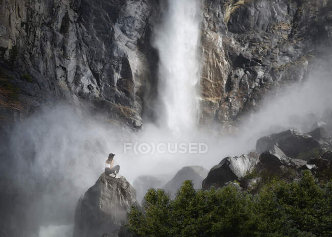 Donna seduta su una roccia alla base di Bridalveil Fall, Yosemite National Park, California, USA — Foto stock