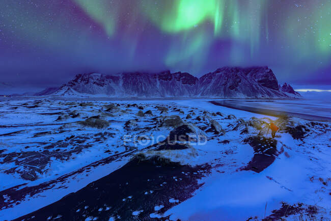 Northern lights over Vestrahorn mountains landscape and distant person, Stokksnes Peninsula, Islândia — Fotografia de Stock