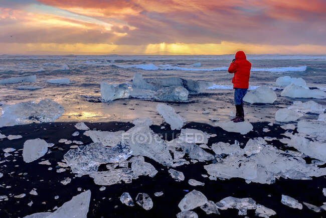 Vue arrière d'une femme prenant une photo au coucher du soleil, Diamond Beach, Jokulsarlon, Parc national des Glaciers Vatnajokull, Islande — Photo de stock