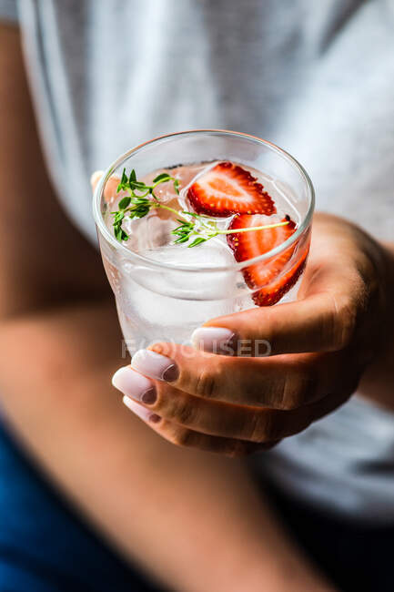 Close-up of a woman holding a glass of ice water with strawberries and thyme — Stock Photo