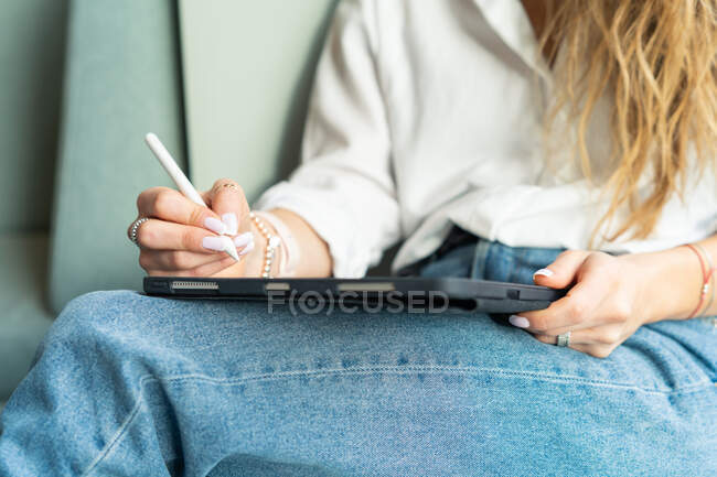 Жінка сидить на дивані, працюючи на своєму планшеті — стокове фото