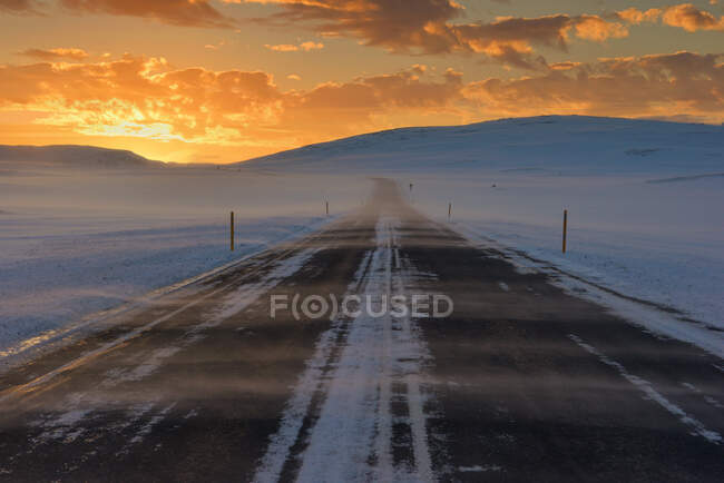 Маршрут через снежный зимний пейзаж на закате, Исландия — стоковое фото