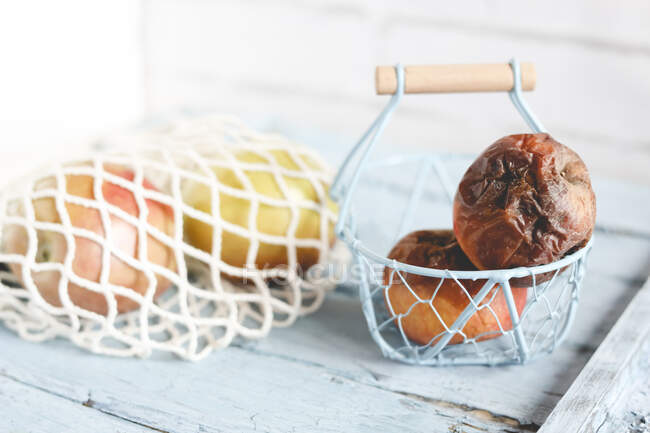 Deux pommes pourries sur une table à côté de pommes fraîches mûres — Photo de stock